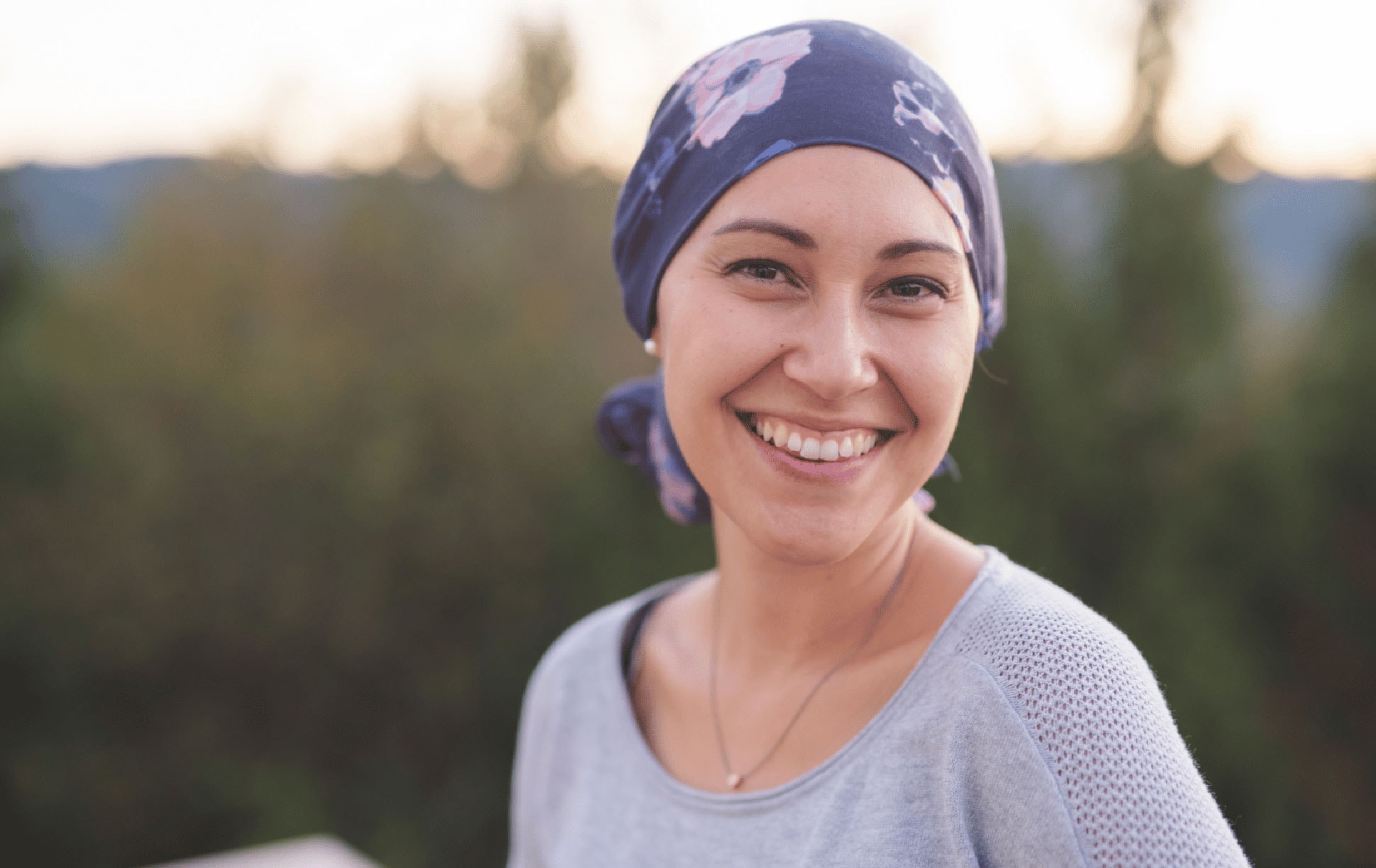 Person wearing a bandana smiling and standing in the outdoors