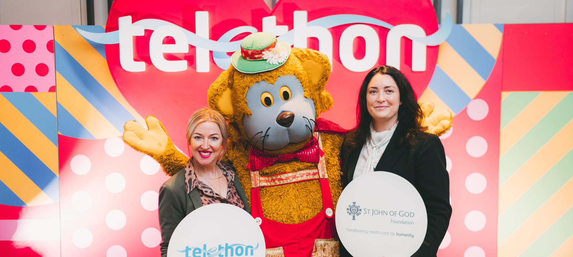 Image of fat cat and St John of God Foundation caregivers in front of Telethon sign