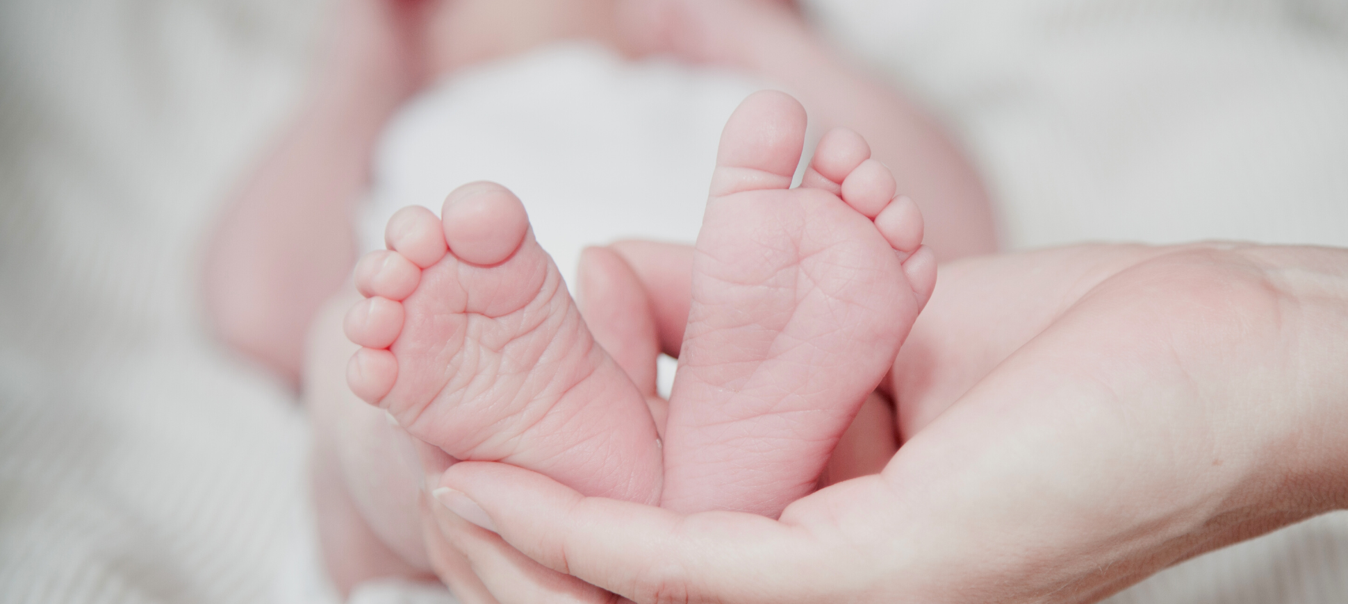 A hand holding a baby's feet as the baby lies down.