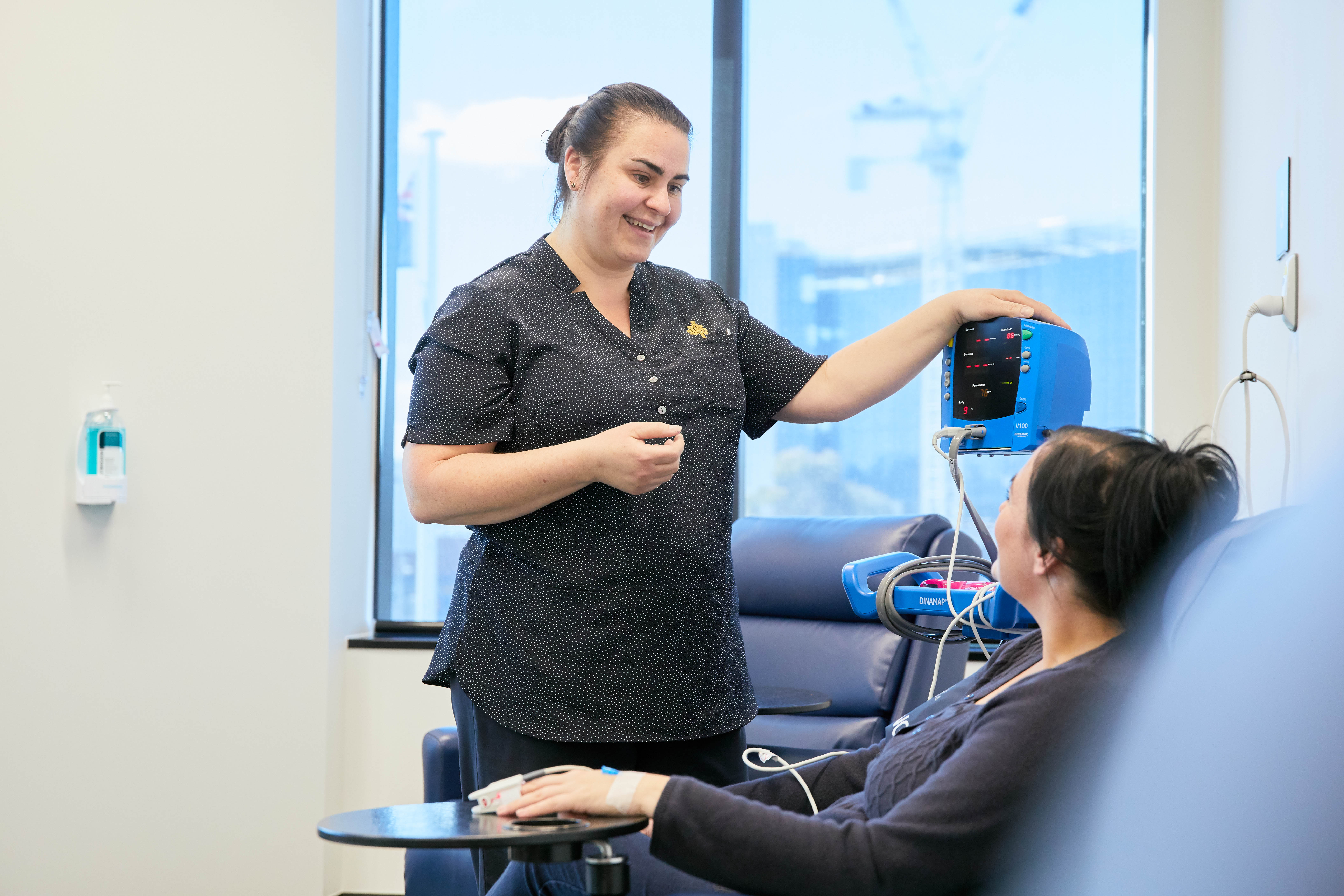 Caregiver smiling at patient and administering an IV. Patient is sitting in a chair