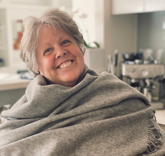 Image of Pauline Tew smiling with a grey blanket wrapped around her